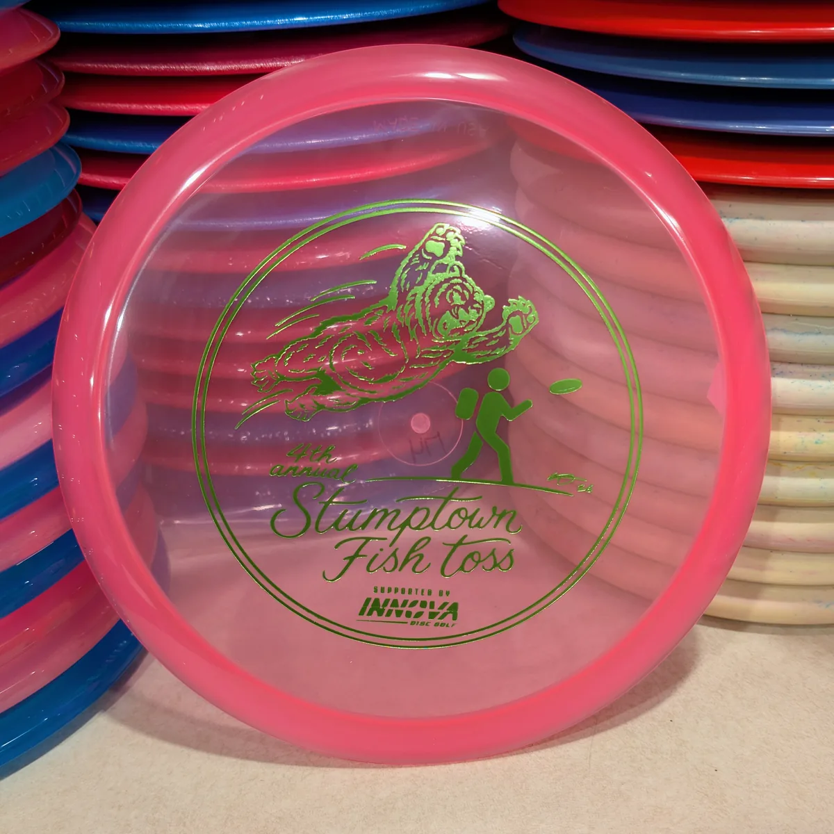 Champion Rollo, clear pink, stamped with the 2026 Stumptown Fish Toss bear, leaning against the disc wall.