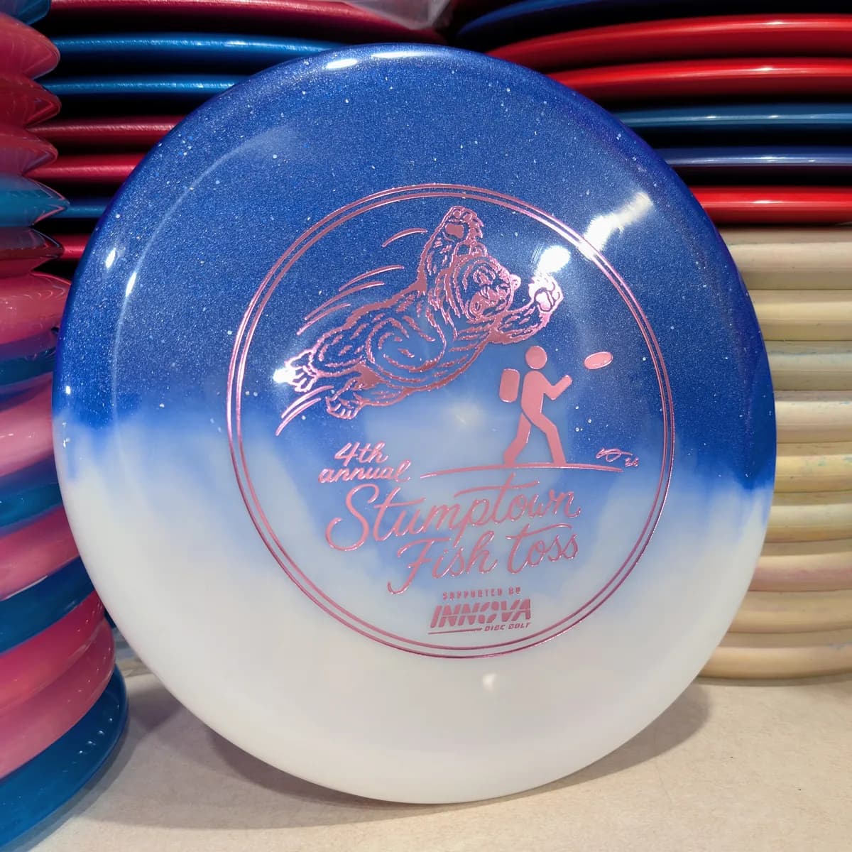 Duo Roc3, blue and white, stamped with the 2026 Stumptown Fish Toss bear, leaning against the disc wall.