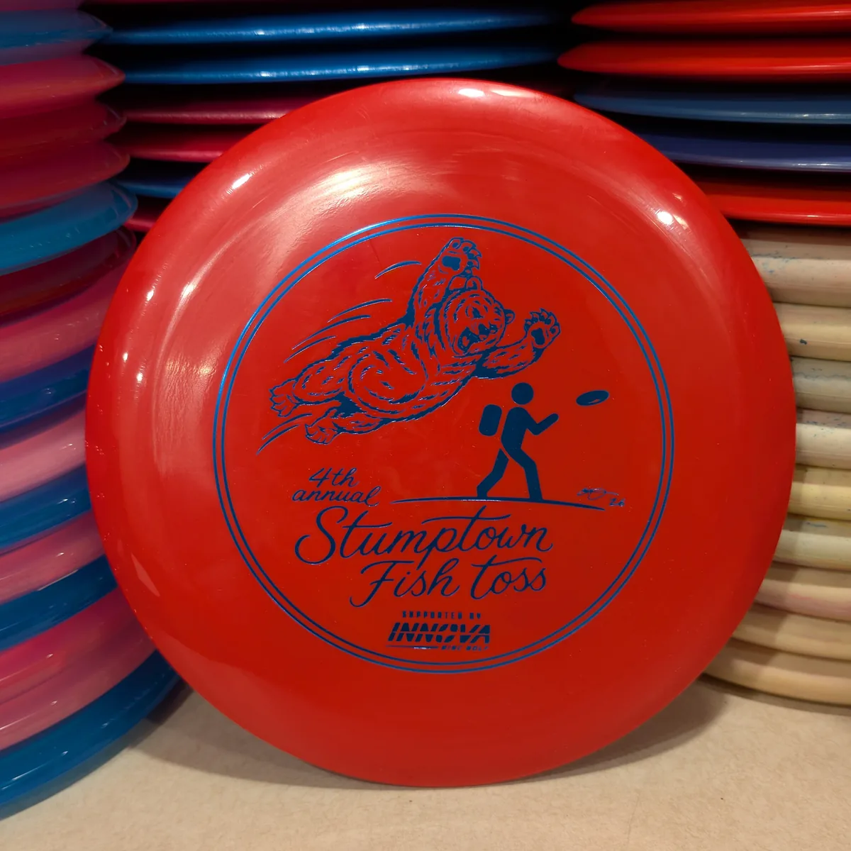 GStar Beast, solid red, stamped with the 2026 Stumptown Fish Toss bear, leaning against the disc wall.