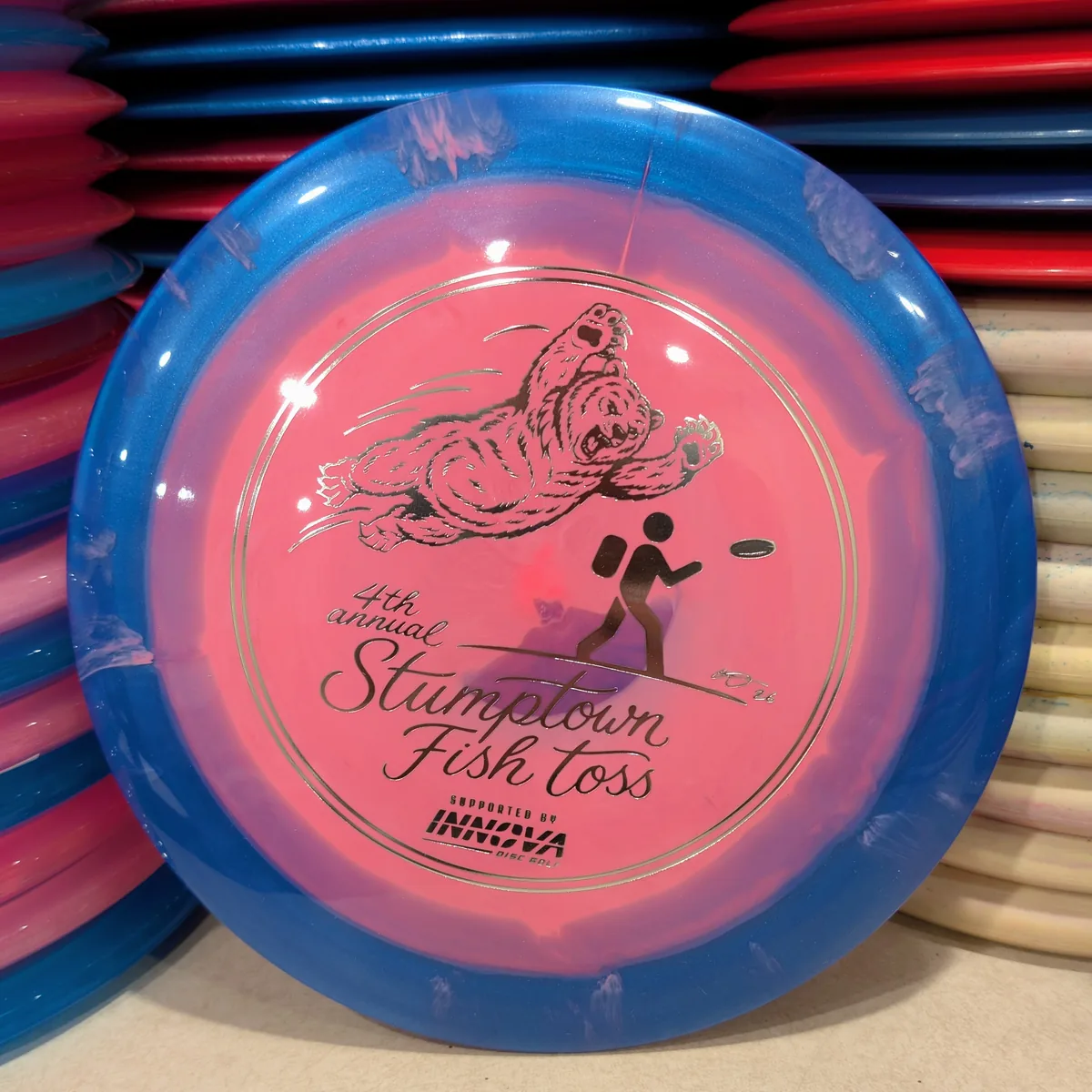 Halo Star Destroyer, pink with a blue rim, stamped with the 2026 Stumptown Fish Toss bear, leaning against the disc wall.