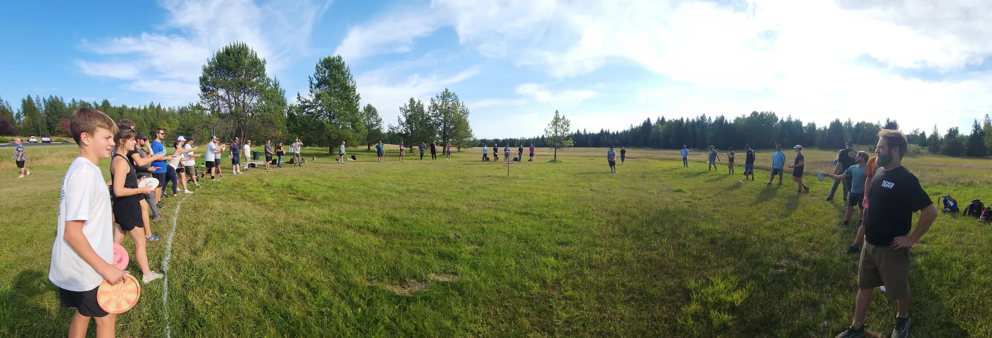 A wide panorama of dozens of players standing in a large circle on a grassy field.